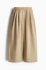 Pantalón color beige de corte holgado con silueta baggy. Modelo de tiro alto con pinzas, elástico revestido en la cintura, cierre y pretina prolongada con botón y corchete ocultos. Bolsillos al bies y bolsillos decorativos atrás.