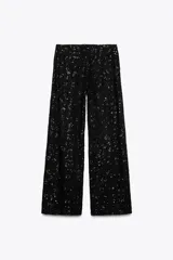 Pantalón negro de tiro alto con lentejuelas, corte palazzo y cierre frontal con cremallera, botón interior y gancho metálico.