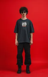 Remera de algodón premium color carbón, corte oversize, con cuello redondo y manga corta. Presenta un estampado frontal con calaveras en estilo caricaturesco, una de ellas con sombrero de copa, rodeadas de humo o nubes, y el texto "CHILLED THE BONE".