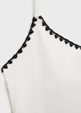 Traje de baño enterizo blanco con ribetes negros, tirantes finos y cuello escotado.