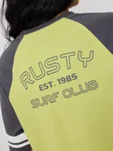 Remera bicolor Rusty con cuerpo verde lima y mangas ranglán grises con dos rayas blancas en los puños. Estampado frontal con el logo de la marca y el número 85.