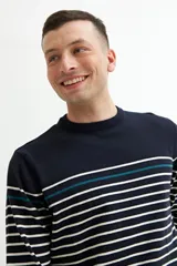 Sweater de punto a rayas horizontales blancas sobre fondo azul marino, con una línea horizontal verde en la parte superior. Cuello redondo, puños y bajo acanalados.