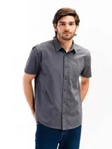 Camisa de manga corta color beige, confeccionada en 100% algodón, con cuello clásico, cierre frontal con botones y bolsillo en el pecho.