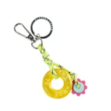 Llavero con aro metálico, mosquetón plateado, cinta de soga trenzada color amarillo flúor y dije circular de acrílico amarillo con la inscripción "XL EXTRA LARGE" y dije de flor rosa con centro celeste.