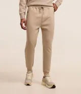 Conjunto deportivo color beige compuesto por un buzo de cuello redondo y un pantalón de jogging con cintura elástica y bolsillos laterales. El buzo es de corte clásico y el pantalón es ajustado en los tobillos.