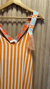 Vestido largo de algodón con rayas verticales naranjas y blancas. Breteles con detalle de bordado floral y flecos.