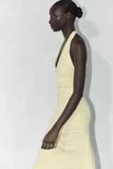 Vestido largo color amarillo pálido, con cuello halter que se ata en la nuca, escote en pico y frunces laterales.