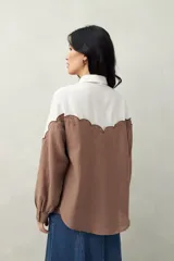 Camisa de lino color crudo y beige, con diseño bicolor y recorte ondulado en el canesú. De silueta relajada, cuenta con mangas amplias y puños camiseros. Se completa con botones de nácar.