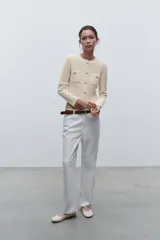 Chaqueta color crema de tejido de punto con cuello redondo y manga larga. Tiene bolsillos delanteros de plastrón y cierre frontal con botones dorados.