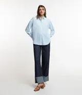Camisa celeste de voile, corte oversized, con cuello clásico, cierre frontal con botones, mangas largas con puños largos y proceso de producción sostenible.