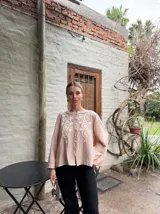 Camisa color beige con bordado floral blanco en el frente y mangas largas. Cierre frontal con botones. Corte holgado.