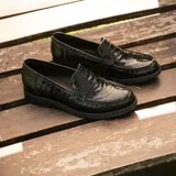 Mocasín de cuero vacuno color marrón, con detalle de antifaz en gamuza. Tiene taco de madera foliado en cuero de 2,5cm y entre suela de goma de 1cm.