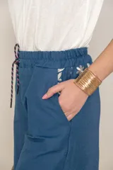 Pantalón italiano de jean azul con bordados florales en color crema. Tiene cintura elastizada con cordón ajustable y bolsillos laterales.