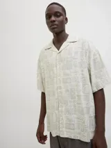 Camisa de manga corta con cuello resort y calce amplio, confeccionada en mezcla de viscosa y lino. Presenta un estampado integral de motivos marinos y botánicos en tonos beige y crema, con cierre frontal de botones.