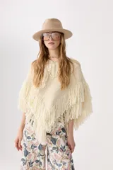 Poncho color crudo de lana merino, con flecos bordados a mano en el ruedo y escote en V.