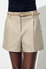 Bermuda color crema de tiro medio con pinzas delanteras y cinturón fino color beige. Tiene bolsillos frontales y falsos bolsillos de vivo en la espalda.