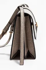 Cartera de hombro tipo sobre, color gris claro, con textura de piel de cocodrilo en relieve. Presenta una solapa frontal asegurada por una tira decorativa con hebilla metálica dorada. Incluye una correa ajustable fina para llevar al hombro.