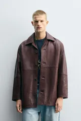 Cazadora de hombre de corte relajado, confeccionada en piel con textura irregular color marrón oscuro (vino/borgoña). Presenta cuello solapa, manga larga con puño abotonado, bolsillos de vivo en cadera, bolsillo interior y cierre frontal con botonadura.