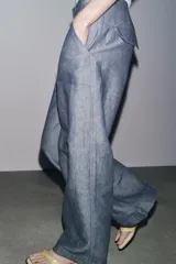 Pantalón de tiro bajo color azul con textura de lino, de pierna ancha, con bolsillos delanteros y traseros. Cierre frontal con cremallera, botón y ganchos metálicos.