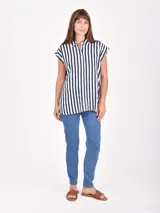 Camisa blanca de manga corta, con cuello camisero y botones frontales. Presenta un corte recto y holgado.