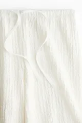 Pantalón recto blanco de punto con textura arrugada, cintura elástica y cordón ajustable.