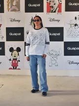 Buzo blanco de manga larga con cuello redondo y puños y ruedo en rib negro. Presenta un gran estampado frontal de la letra 'M' rellena de dibujos de personajes de Disney, incluyendo a Mickey Mouse. Las mangas tienen dos franjas negras a la altura del bíceps.