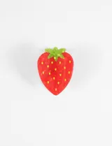 Broche para el pelo con forma de frutilla realizado en PVC. Presenta un diseño en color rojo con puntos amarillos y detalle de hojas verdes en la parte superior.