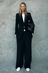 Blazer negro largo con cuello solapa, manga larga con hombreras, bolsillos delanteros de vivo y cierre frontal con un botón.
