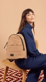 Mochila color beige con diseño capitoneado en la parte superior y tejido tipo telar en la parte inferior. Tiene un bolsillo frontal amplio, asas ajustables y compartimento para ipad.
