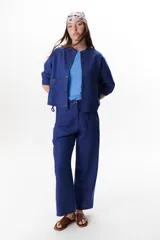 Chaqueta color crudo de lino con cuello redondo, manga tres cuartos, cierre frontal con botones y bolsillos de parche. Detalle de costuras en contraste color marrón.