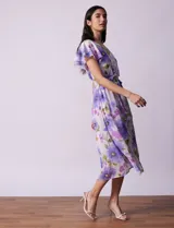 Vestido midi de gasa estampada con flores violetas y verdes, escote en V, abertura central con botones, cintura con lazo de ajuste y forro interno a tono.