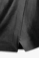 Mono corto negro de efecto piel, con cuello redondo y sisa. Presenta un corte cruzado en el delantero, costuras marcadas y cierre trasero con cremallera.