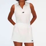 Conjunto deportivo New Balance de tenis para mujer, compuesto por un top sin mangas con cuello polo y una falda corta con cintura ancha. Ambos en color blanco con logo de la marca en azul marino.