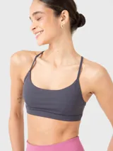 Top deportivo gris de soporte bajo, ideal para pilates y yoga. Tiene escote redondo, tirantes finos ajustables que se cruzan en la espalda y almohadillas removibles.