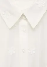 Camisa blanca semitransparente con bordado de flores blancas, de manga corta y cuello camisero.