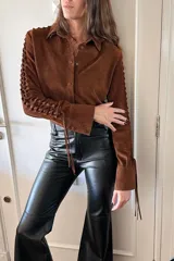 Camisa marrón de gamuza con cuello clásico, cierre con botones a presión y mangas largas con detalles artesanales calados.