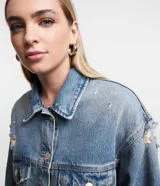 Campera cropped de jean celeste con cuello solapa, cierre frontal con botones, mangas largas, barra deshilachada con flecos y detalles de roturas.