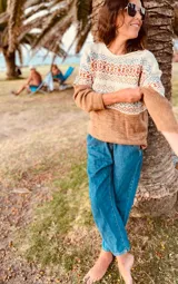 Sweater de lana merino color tostado, con cuello redondo y mangas largas. Presenta un diseño geométrico con motivos étnicos en tonos beige, azul y naranja.