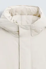 Parka color crudo de tejido técnico acolchado, con cuello alto y capucha ajustable. Tiene mangas largas con puños ajustables, bolsillos frontales con solapa, bolsillo interior y cierre frontal con cremallera oculta por solapa con botones a presión.