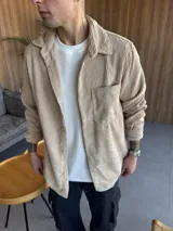 Sobrecamisa color beige de pana con cuello clásico, cierre frontal con botones, manga larga con puños abotonados y bolsillo de parche en el pecho.