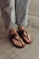 Sandalias marrones de cuero con tiras, microtachas doradas y hebilla lateral.