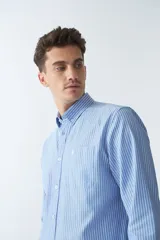 Camisa oxford celeste con rayas verticales blancas, de manga larga y corte regular. Tiene cuello abotonado, bolsillo en el pecho y logo bordado.