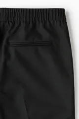 Pantalón negro de sarga con cintura elástica y cordón ajustable, corte slim fit, largo tobillero y dobladillo en el bajo.