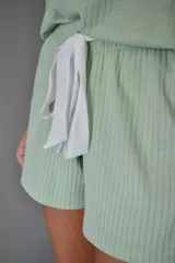 Pijama de short y musculosa color celeste con textura acanalada. La musculosa tiene escote en V con detalle de puntilla blanca y tirantes finos blancos. El short tiene elástico y lazo blanco en la cintura.