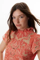 Blusa color coral o terracota con bordado calado floral en tono beige claro. Presenta cuello alto con volado y mangas cortas abullonadas.