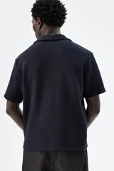 Camisa azul marino de manga corta en tejido de punto con textura. Tiene cuello resort, tapeta con botones y corte recto.