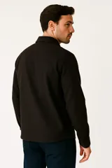 Camisa gris jaspeado de poliéster con cuello solapa, cierre frontal con botones negros, dos bolsillos de parche en el pecho y mangas largas.