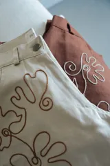 Pantalón slouchy tiro medio color beige con bordado floral marrón.