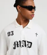 Remera boxy de mangas cortas confeccionada en algodón negro, con cuello polo y estampado frontal con el número 93, la palabra MAD en estilo gótico y una cruz. El algodón es certificado BCI.