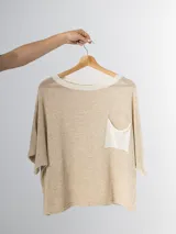 Remera tejida en hilo italiano, color beige, con cuello a la base y bolsillo frontal. De caída relajada y silueta amplia.